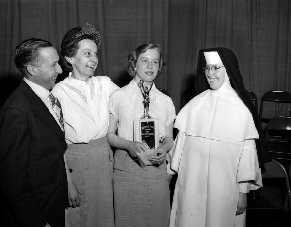 Spelling bee champion Arlene Brown of Janesville holding her trophy.  Smiling on the right is her eighth grade teacher at St. Mary's Catholic school, Sister Mary Dalmatia. On the left, Arlene's parents, Mr. and Mrs. Verne Brown are looking on proudly.