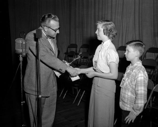 Roy L. Matson, editor of the <i>Wisconsin State Journal</i>, gives a handshake to champion Arlene Brown of Janesville as runner-up Dale Sorenson looks on.