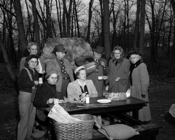A group portrait of the officers of the Wisconsin Outers enjoying a picnic at Hoyt Park despite the chilly weather. Pictured left to right in the foreground are: Dagney Borge and Daisy Border, editors of the club bulletin and Dr. Ruth R. Harmon, past president. Standing in the background left to right are: Carol Bird, secretary; Max Lindemann, treasurer; F.W. Huels, past president; Mrs. Charles H. (Alice) Hemingway, president; and Bertha Frautschi, vice-president.