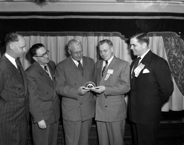 Group portrait the officials of the Wisconsin Retail Jewelers Association, and Governor Oscar Rennebohm, the main speaker at their convention, held in the Hotel Loraine in Madison. Pictured left to right: B.W. Heald, Milwaukee, secretary; Harry Blum, Madison, convention chairman; Governor Rennebohm; A.C. Hentschel, Milwaukee, president; and Arlie Mucks, Jr. Madison, entertainment and banquet chairman. Mr. Hentschel is shown presenting a watch as a gift to Governor Rennebohm.