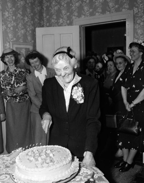 Miss Flora Mears, 116 East Gilman Street, cuts a birthday cake provided by the members of the Madison Art Guild of which she was an active member for many years. Miss Mears had invited guild members to her home and had no idea the event would turn into a surprise birthday party.