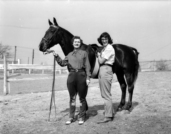 Joan Kaye (left) of Whitefish Bay, Wisconsin, and Beverly Kaplan of  Sioux City, Iowa, participants of the Hoofers' horse show, saddle a horse, "Her Highness."