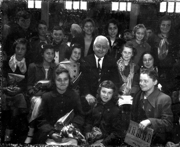 Professor E.B. Gordon is shown surrounded by some of his 90,000 "radio children," 3,500 of whom sang for him Saturday at the University of Wisconsin stock pavilion. These youngsters are from the Frank Allis School.