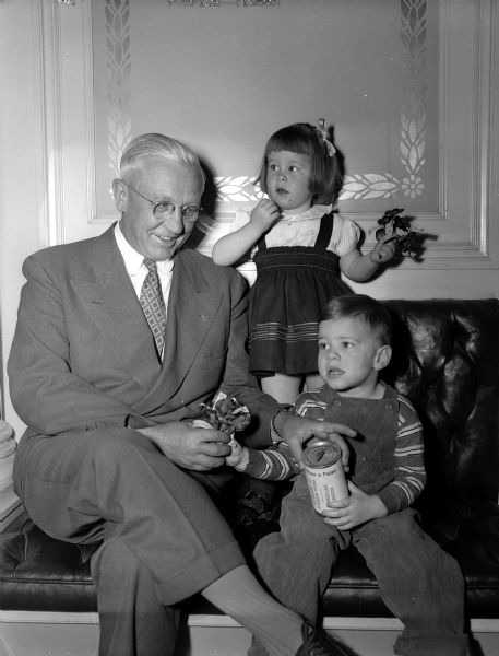 Governor Oscar Rennebohm receiving the first poppy of the year from Patty Coyne, daughter of Dr. and Mrs. J.J. Coyne and Phillip Thornton, son of Mr. and Mrs. Melvin A. Thornton. The annual poppy sale is sponsored by the American Legion and the Veterans of Foreign Wars.