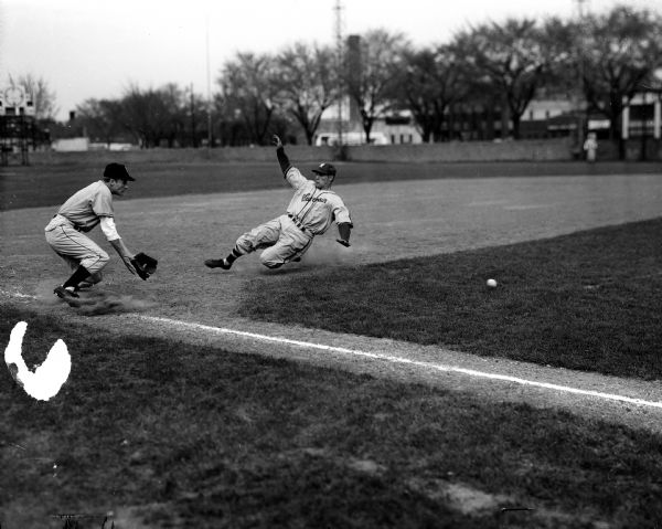Ernie Bauer (Wisconsin) slides into third base while Gerold Dorr waits for a throw from first baseman during a University of Wisconsin vs. University of Michigan baseball game.
