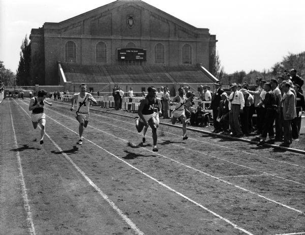 The only winner of three individual events in Saturday's triangular track meet at Camp Randall was Northwestern's Jim Holland, shown here winning the 100 yard dash. It was the first of his victories. Left to right and the places they won are: Walker Reid of Wisconsin, fourth; Bill Konrad of Michigan, second; Jim Englander of Wisconsin, third, and an unplaced Michigan runner.