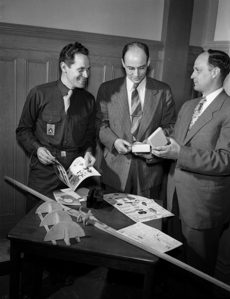 Three members of the camp advisory committee of the Community Welfare Council, sponsor of Madison's first Camp Week, look at literature and materials displayed on a table. From left to right are: Don Bezucha, director of Camp Tichora boy scout camp; Kenneth E. Kitchen, chairman of the advisory committee; and Marvin Lotz, director of Camp Wakanda YMCA camp.