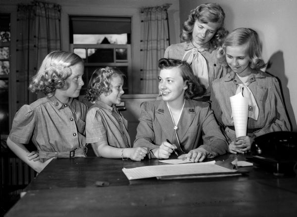 Four Girl Scouts and Brownies register for summer camps with Mrs. Mary Grindrod, a member of the scout staff. The girls are, from left: Roxie Ann Bjelde, Barbara Petersen, Faye Jorgensen, and Judith Briggs.