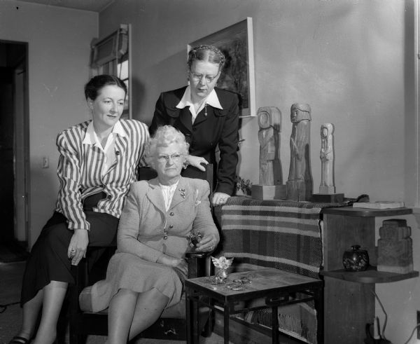 Three Madison women and a display of their crafts. The women, members of the Wisconsin Designer-Craftsmen Society, and their crafts are: Mrs. Bentley (Leanora) Courtnay, Christmas angel jewelry set; Mrs. Irving T. Severance, wood sculpture and iron table; and Ruth Harris, weaving. They are meeting in the Severance home on Merrill Springs Road.