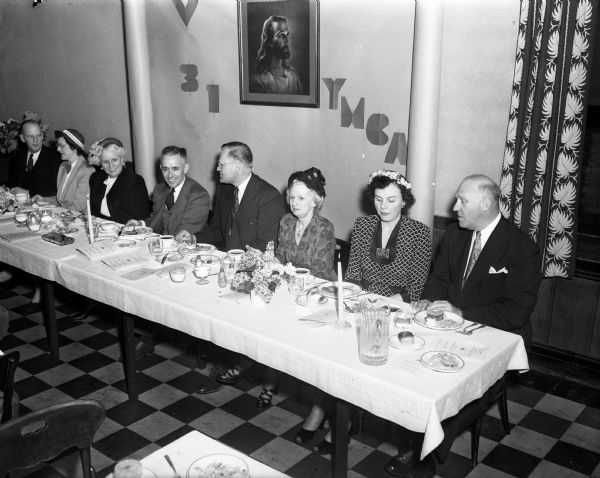 Men and women sitting at the speaker's table during the YMCA's 31st Annual Meeting. Pictured, left to right, are: the Rev. Alfred B. Swan, pastor of the First Congregation church, Mrs. Cecil (Janice) Lower; Mrs. Milton (Leona) Findorff; the Rev. Cecil W. Lower, pastor of the University Presbyterian Student church and principal dinner speaker; Edwin O. Rostsen, secretary of the board and toastmaster; Mrs. Alfred (Eva) Swan; and Milton B. Findorff, president of the board.