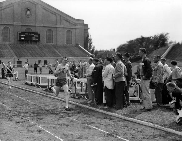 Jack Mansfield, West High School, crosses the finish line as winner in the Class A 440 yard dash in the WIAA State Track meet. In the background is the University of Wisconsin-Madison Field House at Camp Randall.