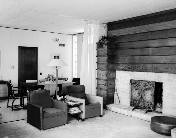 Interior view of the Porter Butts house at 2900 Hunter Hill in Shorewood Hills, one of the first "modern" houses in the Madison area, built in 1937. The sandstone fireplace is featured, set in a wall of redwood paneled horizontally. A yellow casement cloth curtain divides the living room from the dining area. Contemporary furnishings are used in both areas.