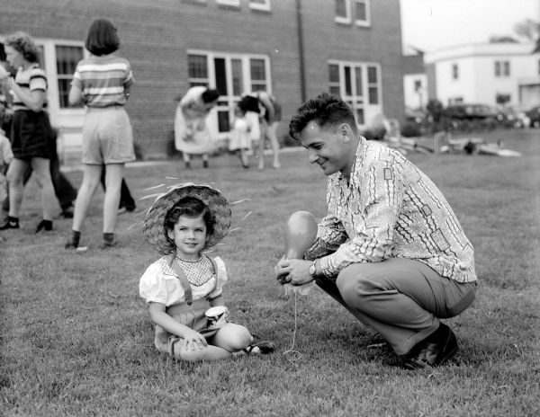 Cynthia Cottam, age 3 and a half, watches as children participate in a parade of gaily decorated tricycles while costumed as Native Americans, cowboys, and flowers.  The parade was followed by ice cream and balloons. Cottam is the daughter of Prof. and Mrs. Grant Cottam of the University of Wisconsin.