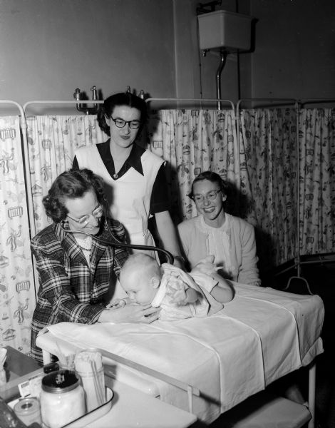 Dr. Ruth Foster, left, is shown examaning baby Janet Lee Sommerville while assisted by Nurse H. Anita Anderson as the mother, Mrs. Robert Somerville, is looking on. They are inside the newly renamed East Washington hospital clinic at the new "well baby" clinic at 1954 E. Washington Avenue and are supervised by the Madison city health department. The building was previously known as the Madison Contagious Hospital.