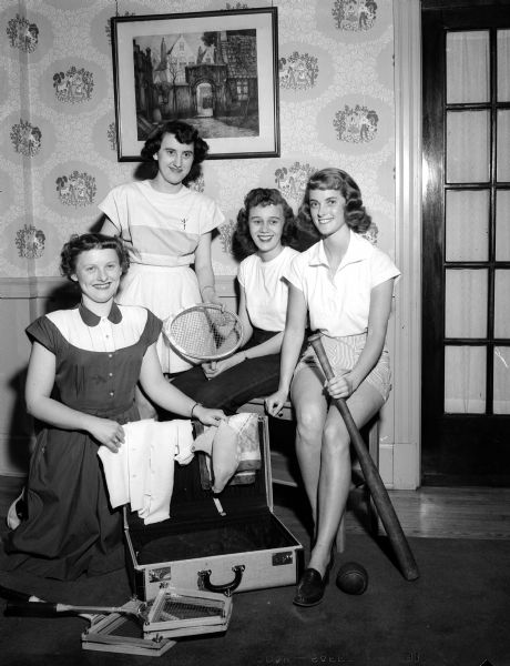 Four young working women who plan to attend the YWCA camp for working girls on Lake Mendota 12 miles from the Capitol are pictured, left to right, with a suitcase and sports equipment: Mary Metcalf, Shirley Kreul, Arletta Attleson, and Phyllis Nickerson.