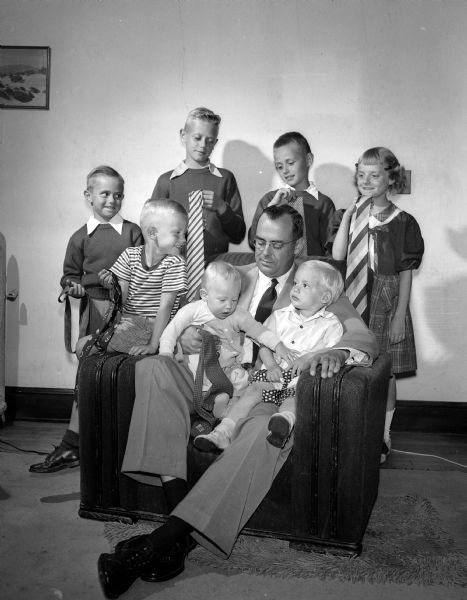 Group portrait of William B. Cantwell and his seven children, each of whom holds a necktie to give him for Father's Day.  Sitting on the arm of the chair at the left is Stephen, age 4, Mr. Cantwell holds the two youngest boys, Thomas, 9 months and Patrick, 2 years.  Standing from left to right are: Roger, 7; Michael, 11; Jeffrey, 10, and the only girl Connie, age 9.
