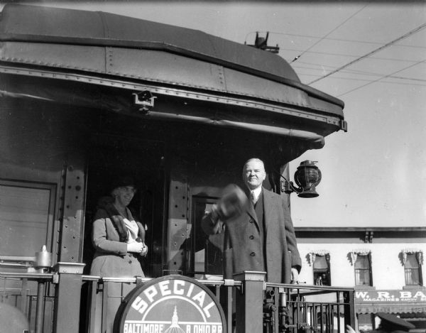 President Herbert Hoover stands with his wife on the platform of their special train as they arrive in Madison. Hoover spoke at the University of Wisconsin fieldhouse.