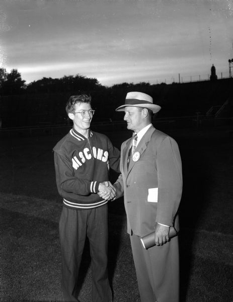 Don Gehrmann (left), who capped a great career by winning the mile and half mile races at the Big Ten-Pacific Coast intercollegiate track meet held at Camp Randall Stadium, shakes the hand of Wisconsin track coach Guy Sundt, who is retiring from his coaching duties to take up his new position as Director of Intercollegiate Athletics at the University.