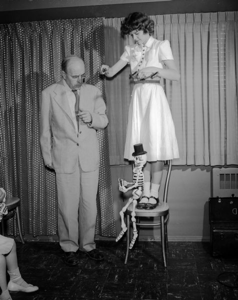 Professor Henry L. Ewbank of the University of Wisconsin speech department admires the marionette "Casper Cadaver" being manipulated by Ethel Miller at the sorority marionette show at the Edgewater Hotel.
