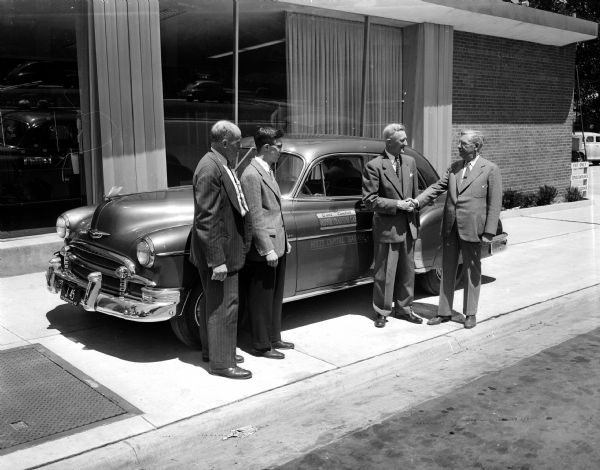 The Madison board of education's summer driving program for high school students acquires another American Automobile Association (AAA) dual control car, a Chevrolet. Pictured with the car right to left are: Philip H. Falk, Superintendant of Madison Public Schools, being congratuated by Ralph Hult, president of Hult's garage and chairman of the Wisconsin Inter-Industries Highway Safety Committee, as E.A. Precourt, supervisor of safety for the Wisconsin AAA, and Lester Levine, president of the Madison Youth Council, look on.