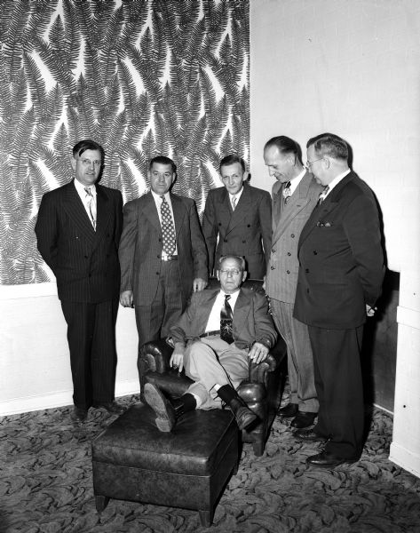 Retiring Kroger Company district manager, Henry M. Zweifel, sitting in an armchair and using an ottoman, both given to him by Kroger employees on the occasion of his retirement.  He is shown with five of his store managers: Stanley Walsh, Dubuque, Iowa; Delos Deiter, Boscobel; Ed Micka, Darlington; Irv Miller, Oshkosh; and Pat Ryan, Prairie du Chein.
