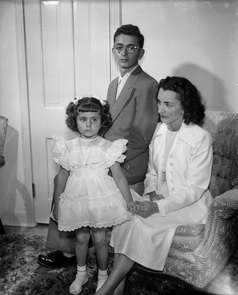 Mrs. Joseph Savone of Sacramento, California is sitting while posing for a portrait with her children Peter and JoAnn. They are visiting Mrs. Savone's sister, Mrs. William (Josephine) Glasser.
