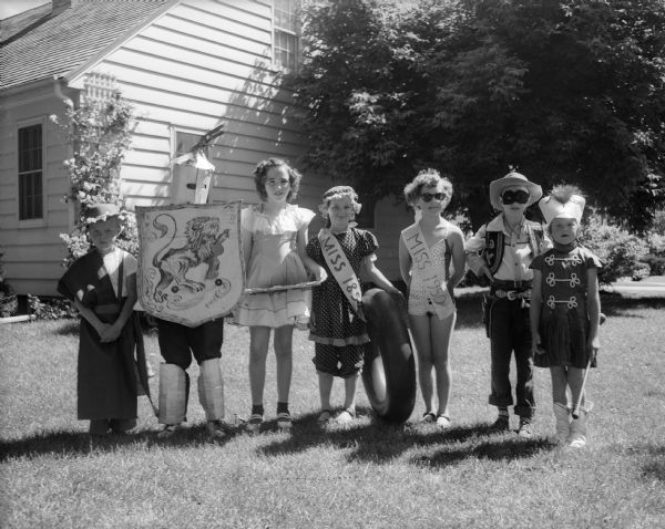 Seven children in costume who participated in one of the most colorful 4th of July parades in village history pose for a portrait on a lawn.
