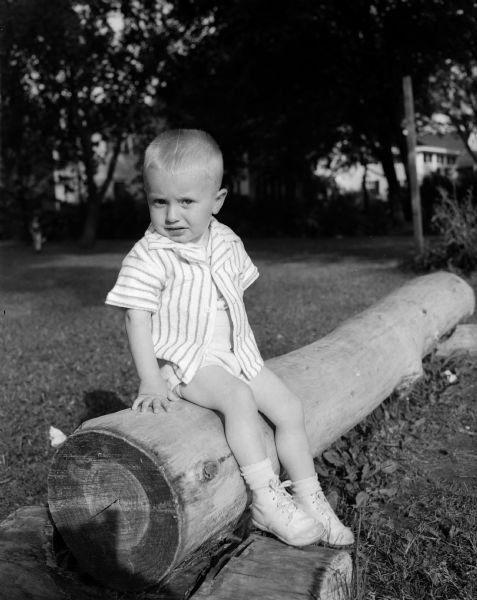 A boy, possibly the son of Edwin and Mary Albright (David), born August 6, 1947, sits on a log for an outdoor portrait.