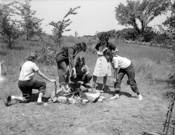 Girl Scouts cook their "campfire stew" at Camp Greenwood, a day camp at Picnic Point for Intermediate Girl Scouts between the ages of 10 and 14.  Pictured from left to right are:  Judy Deans, Jean Bell, Cynthia Eccles, Deloris Heinz, and Jane Craig.