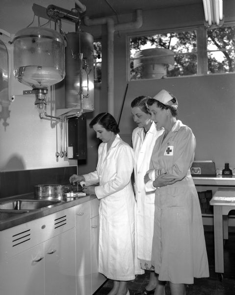Dr. Merle Owen Hamel (left), American Red Cross Blood Center physician, shows features of the center laboratory to Mrs. John Brown, volunteer representing the Dane County Medical auxiliary, and Mrs. William E. (Julia) Walker, one of the Gray Ladies serving as hostesses at the center.