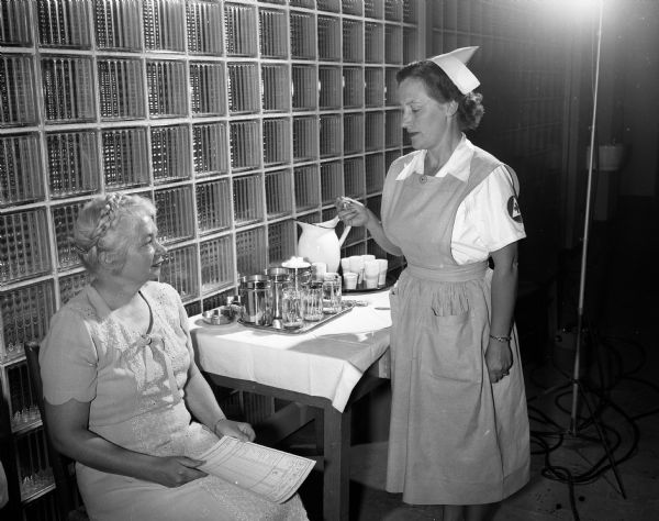 Mrs. John (Emily) Sprague, right, nurse's aide at the American Red Cross Center blood bank, preparing to take the temperature of blood donor, Mrs. Richard (Lucille) Butler.
