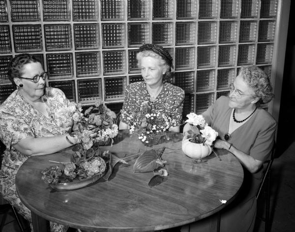 Three Garden Club members arrange flowers at the American Red Cross Blood Center. Left to right: Mrs. T.H. Davies, president of the Madison District of the  Wiconsin Garden Club Federation; Mrs. R.O. (Helen) Wissler, president of the Sunset Garden Club; and Mrs. A.C. (Margaret) Garnett, president of the West Side Garden Club.