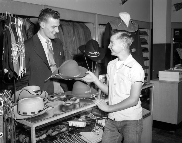 LeRoy Young, 1204 Lakeview Avenue, a Madison Soap Box contender, at the Hub Clothing Store, his sponsor for the race. Jim Schmitz, a store clerk, is showing him a Hopalong Cassidy hat.