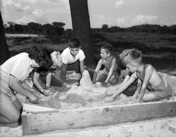 Six children are shown playing and building sand castles in a sand box at Penn Park.  Left to right, they are Dulcie Snell, Tommy Smith, Joe Valenza, Tony Scalissi, Mack Snell (hidden) and Bill McCann.