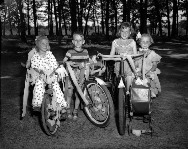 Four children with three decorated bicycles and a doll buggy at Gallagher Plat playground.