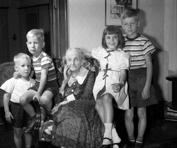 Mrs. L.L. (Olivia Douglass) Se Cheverell sitting in a chair while surrounded by four great grandchildren. She is celebrating her 100th birthday.