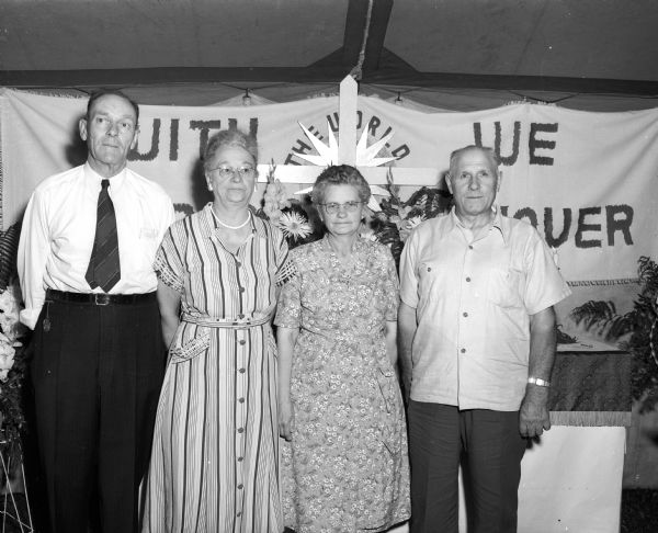 Probably a photo of the first two couples to be married at Zion Lutheran Church standing in front of a banner at the picnic celebrating the church's 50th anniversary. They are Mr. and Mrs. Arthur Malsch and Mr. and Mrs. Henry F. (Flora) Schultz.