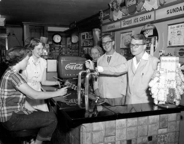 Madison teenagers J. Ludger Parr and Jim Graham dispense cokes to Carma Rae Chapman and Sheila Ryan at a local drug store as they work at their summer jobs.