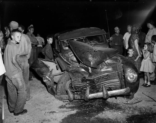 A crowd of onlookers surrounds a wrecked automobile. The accident occurred at Highway 30 and North Fair Oaks Avenue.