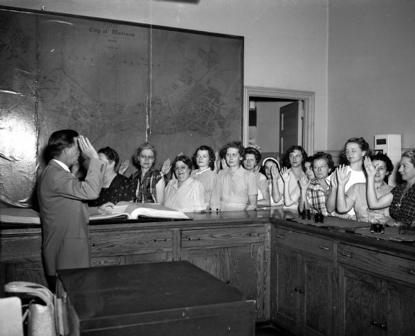 Volunteers who will staff five special voters registration centers during "Register and Vote week" are shown being sworn in by City Clerk Al W. Bareis at left. Volunteers left to right: Mrs. Frieda B. Luloff, Mrs. Ruth Day, Josephine S. Brahm, Mrs. Maybelle Moore, Mrs. Stanley (Esther) Ashby, Mrs. Lewis R. Williams, Mrs. Natalie L. Spector, Mrs. Fred (Florence) Raemish, Mrs. Sidney (Marrian) Schwartz, Dr. Ruth R. Harmon, Mrs. George (Mary) Reinke, Mrs. Frieda S. Cohn, and Mrs. Rosalie Zimmerman.