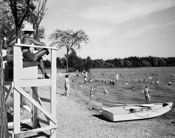 A lifeguard observes swimmers at the beach in Vilas Park. A rowboat used by the lifeguard is on the beach.