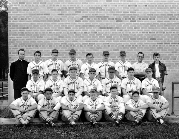 Group portrait of twenty uniformed members of St. John's baseball team, Waunakee, Dane County's Catholic Youth Organization League championship team, along with a priest, a manager, and a batboy.