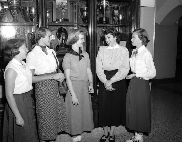Five Madison High School students gather at the trophy case at East High School. Left to right are: Lee Miller, Edgewood; Nancy Fowlkes, Wisconsin High; Norma Malmanger, Central; Nancy Fay, West; and Barbara Bruley, East.