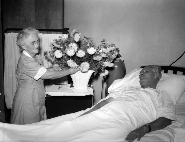 Mrs. E.M.(Mary) Lynch, volunteer, arranging flowers and visiting with W.K. Loughborough in a patient room at St. Mary's Hospital. Flower delivery is one of the many volunteer activities aiding the nursing staff.