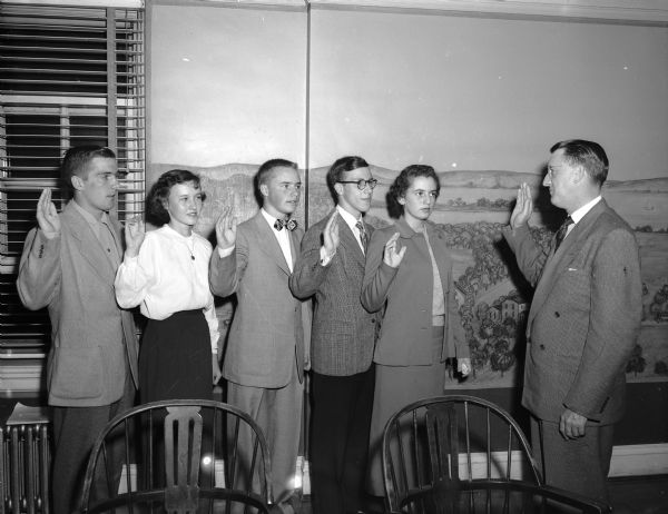 New officers of the Madison Youth Council are sworn in by city Clerk A.W. Bareis in the Old Madison Room of the Memorial Union. Left to right are: John McCormick, treasurer; Lois Brustman, vice-president; Stefan Anderson, corresponding secretary; Lester LeVine, president; and JoAnne Gilbert, recording secretary and Bareis.
Nearly 70 delegates and advisors from Youth Council member agencies, local high school principals and Council adult advisors attended the meeting.
The Reverend Robert Borgwardt, pastor of the Trinity Lutheran church, gave the invocation, Adult advisors who helped plan the dinner were Mrs. John (Joanne) Bloomer, LeRoy Luberg, Dr. H.T. Scott, Robert Beck, and Kenneth Orchard.