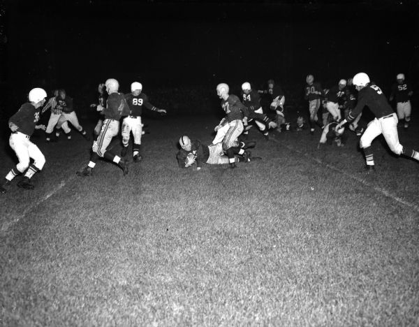 East High School fullback Jim Kurth (#32) on ground, stumbled to a halt at the Madison East-Janesville game at Breese Stevens Field. Shown next to Kurth is Guard Dale Pollock (27) of East High School.  Also shown is Tackler Charles Gray (54) of Janesville. Score: Madison East 13, Janesville 0.