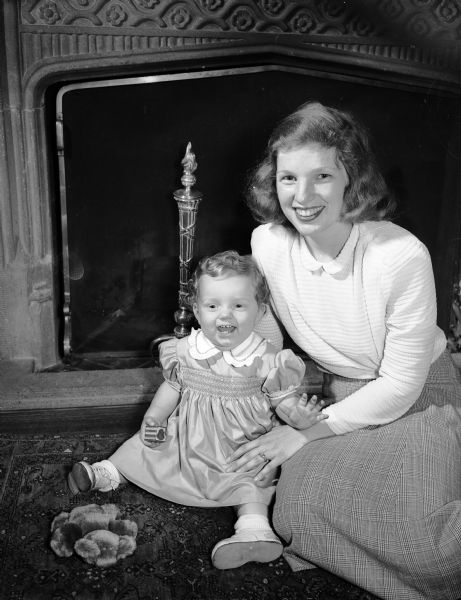 Mrs. Oliver M. (Carol Sisk) Patterson, of Fox Lake, Illinois sitting near a fireplace with her daughter, Alison, during a visit with her parents Mr. and Mrs. Ira Sisk.