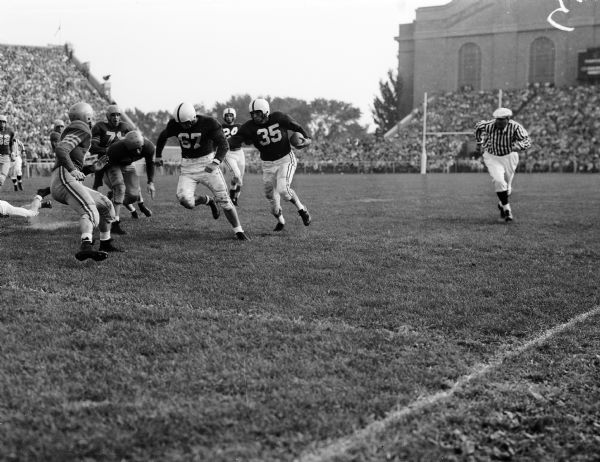 Badger Halfback Bob Mansfield makes a first down with help from Guard Bob Kennedy (#67).
