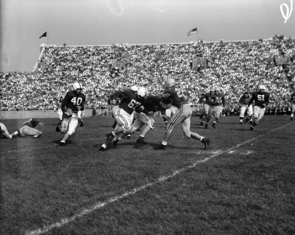 Wisconsin guards Ken Huxhold (#70) and Bob Kennedy (#67) clear the way for halfback Rollie Strehlow (#40) against Marquette in their game at Camp Randall Stadium.
