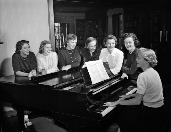 Pledges of the Delta Gamma sorority gather around the piano as Harriet Kirchhoff sits on the piano bench to play. From the left are: Joan Sexton, Madison; Mary Sisk, Madison; Virginia Bowman, Fox Bluff; Rosamond Ross, Madison; Joan Grove, Madison; and D'Arcy Timmons, Madison.